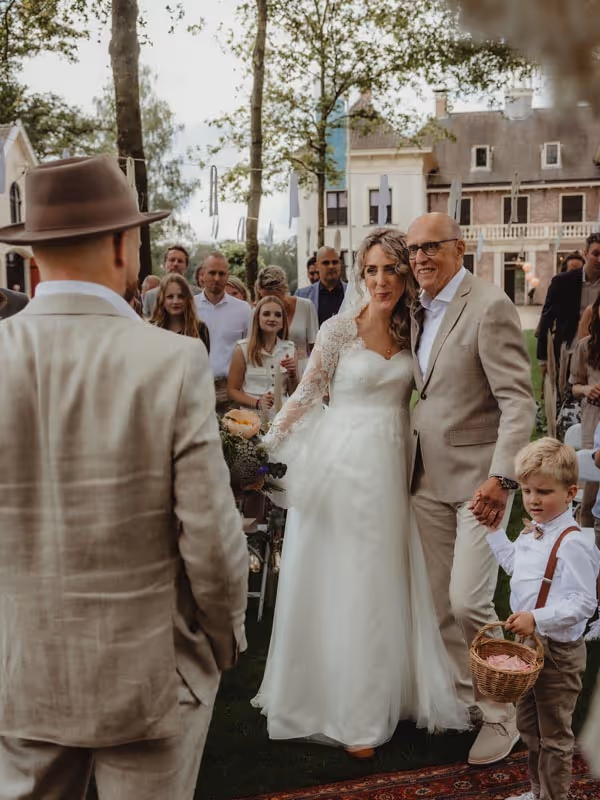Bruid die aankomt lopen met vader en bruidsjongen richting bruidegom