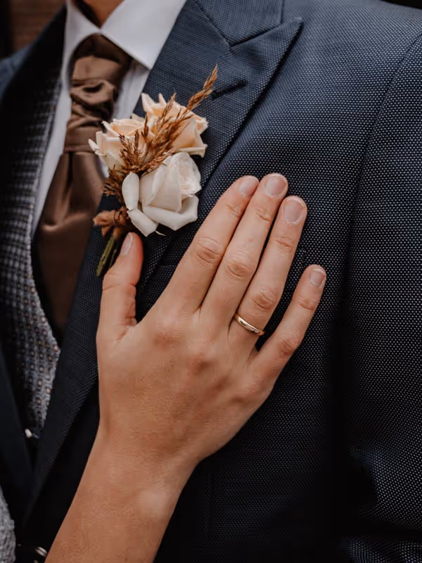 Close up corsage bij bruidegom met hand van de bruid en haar trouwring