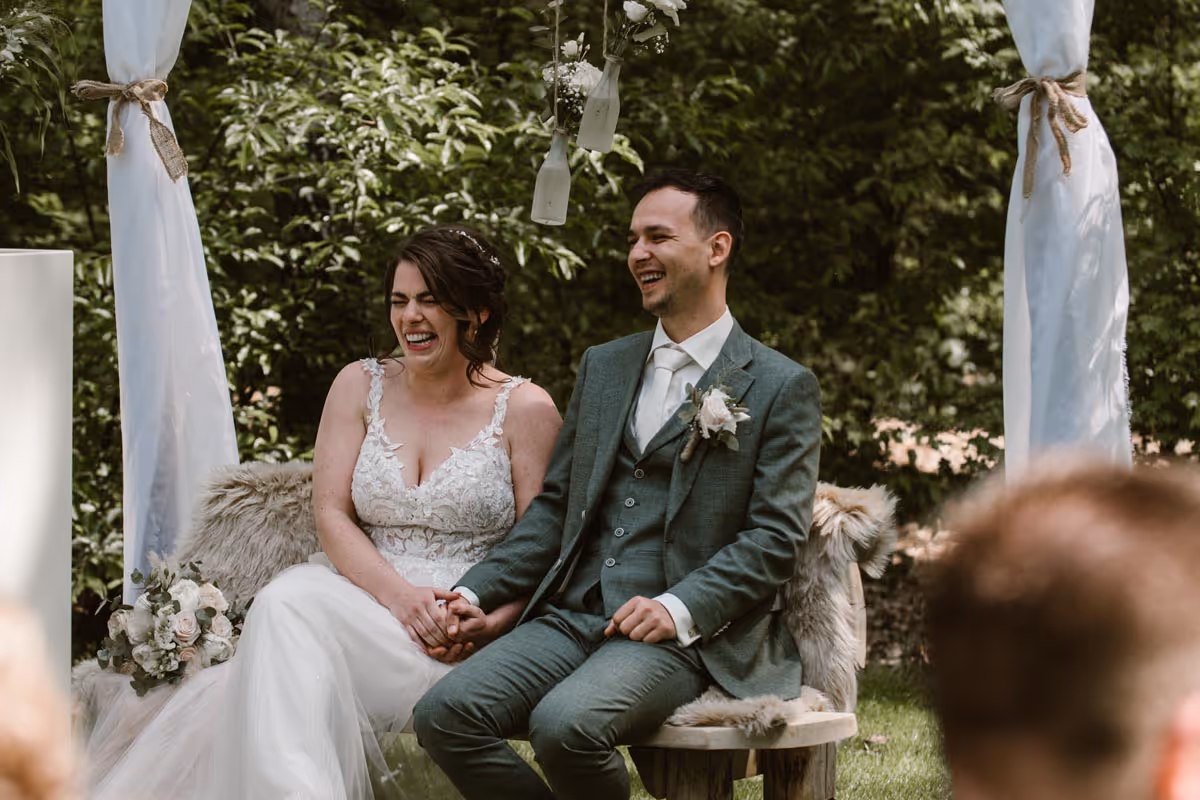 Lachend bruidspaar tijdens ceremonie op het trouwbankje