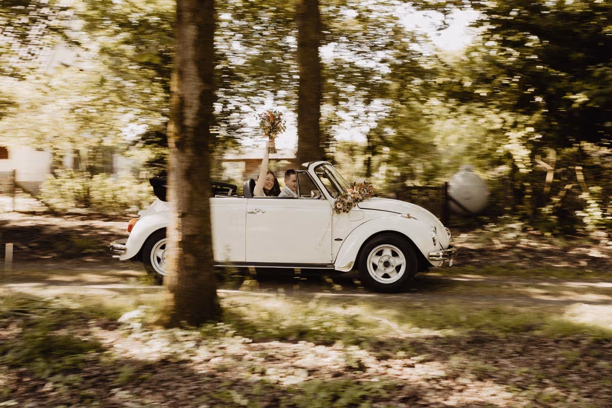 bruidspaar rijdend in trouwauto een witte kever cabrio, de snelheid/beweging in de omgeving is moois vastgelegd