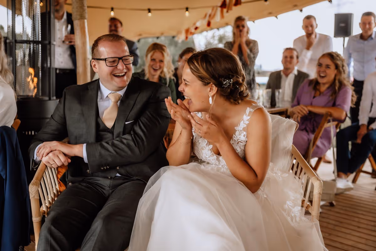 schaterlachend bruidspaar op trouwbankje tijdend ceremonie