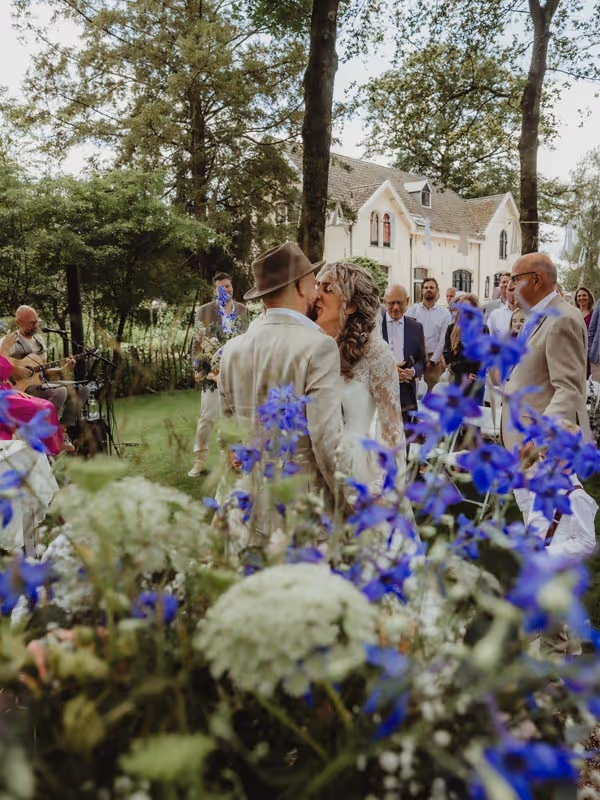 Bruidspaar wat elkaar een kus geeft met mooie blauwe bloemen op de voorgrond