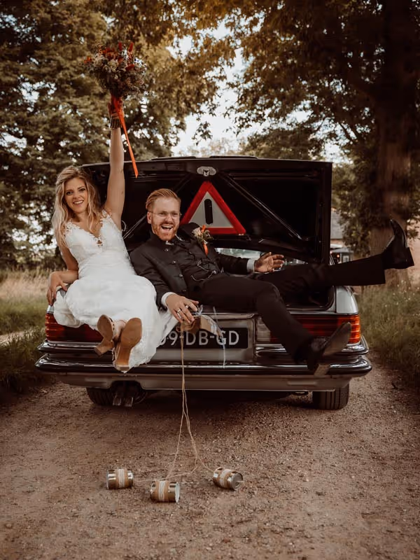 Bruid en bruidegom in de kofferbak van trouwauto met blikjes er achter